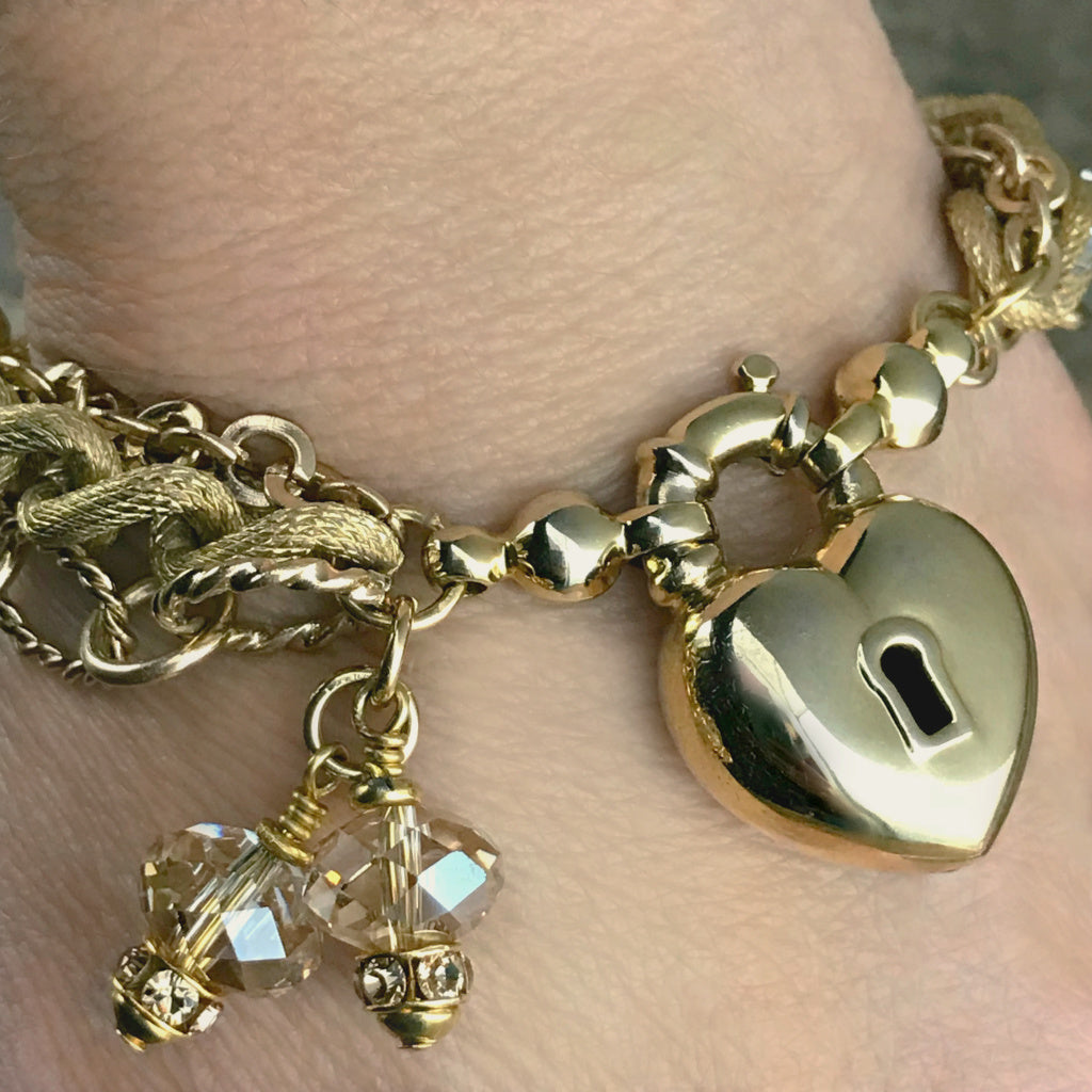 ​​​The soft gold color of this Suzie Q Studio one-o​f​-a-kind bracelet, along with the sparkle of Swarovski crystals, three styles of chain and unusual heart-shaped focal closure, provides an elegant, show-stopper look