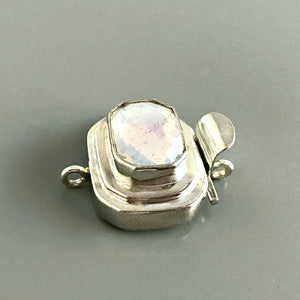 This Suzie Q Studio custom box clasp was handcrafted with a rectangular, white opalescent, vintage glass cabochon and set in sterling silver. The finish of the glass piece used in this closure is distressed, and along with the faceting and cut corners of the rectangle shape, contributes to its beautiful antique feel. 