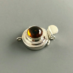 This Suzie Q Studio custom box clasp was handcrafted with a round, amber-style, vintage glass cabochon and set in sterling silver. The swirl of dark brown in the centre of a pool of maple syrup coloured glass gives this box clasp a decided look of real amber!