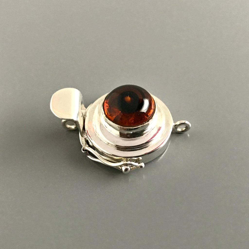 This Suzie Q Studio custom box clasp was handcrafted with a round, amber-style, vintage glass cabochon and set in sterling silver. The swirl of dark brown in the centre of a pool of maple syrup coloured glass gives this box clasp a decided look of real amber!