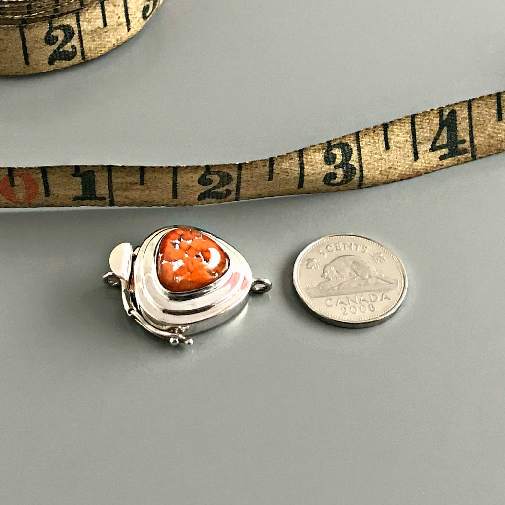 This Suzie Q Studio sterling silver custom box clasp is a very unusual and distinctive closure. The triangle shape of this vintage glass cabochon coupled with the mottled, burnt orange color on a base of silver “leaf”, showcases a retro-1950’s feel as well!