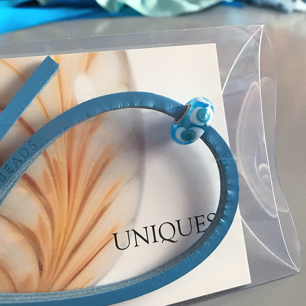 Trollbeads UNIQUES are one-of-a-kind glass beads handmade individually by 100% artisan-owned workshops. The colour and design of this Suzie Q Studio UNIQUES glass bead looks like waves at the beach.