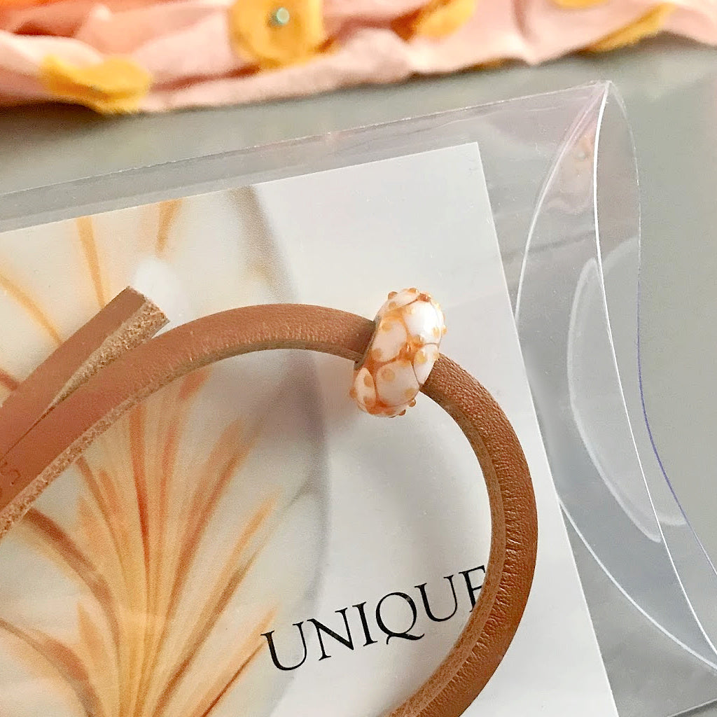 This sweet confection of a bead on Suzie Q Studio Trollbeads UNIQUES glass bead bracelet looks like honey on waffles and has a colour-coordinated leather bracelet. UNIQUES are great layered on your wrist and make wonderful gifts!
