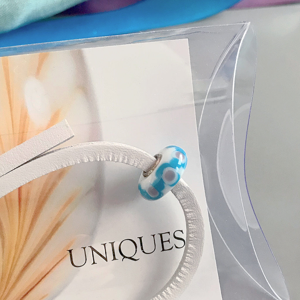 Trollbeads UNIQUES are individually handmade, one-of-a-kind glass beads. This stunning Suzie Q Studio UNIQUES glass bead features the striking colours of a tropical island vacation with a white leather bracelet.