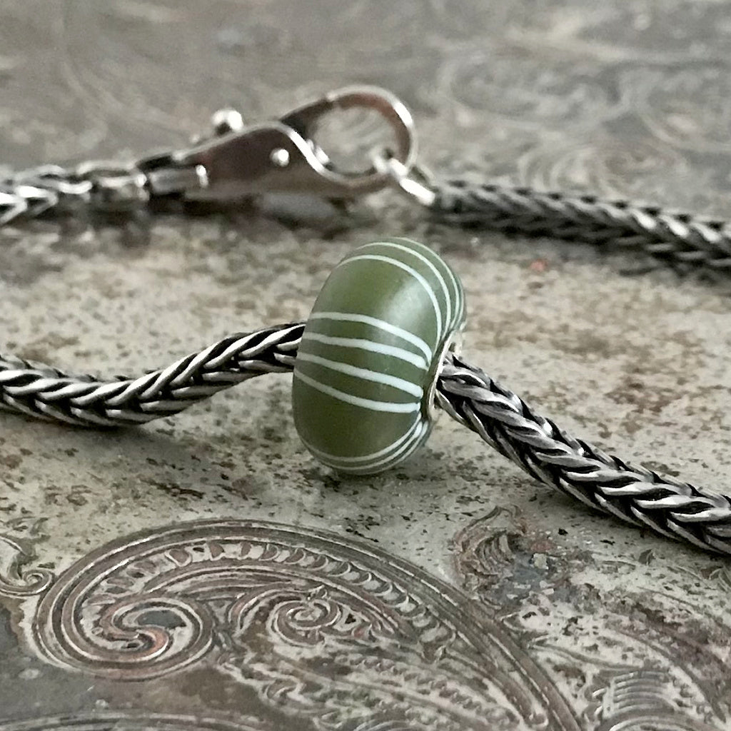 Suzie Q Studio's exquisite Kimono "Seigaiha" matte green Trollbeads limited edition glass bead was originally part of a set of six beads called the “Kimono Kit". This ultra-rare bead was not only designed by a Japanese designer, but it was also made from Japanese glass. It's inspired by the color and pattern of a Japanese silk kimono.