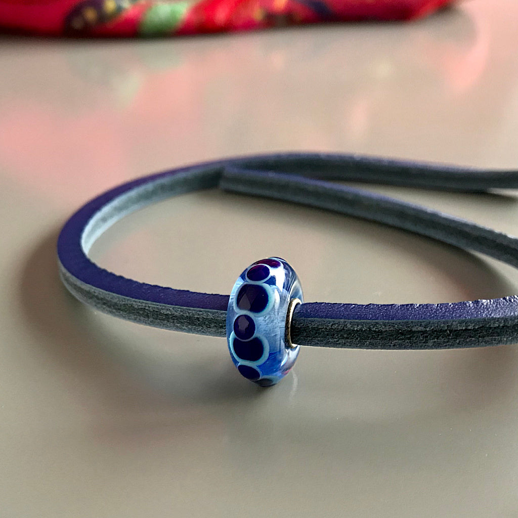 Trollbeads UNIQUES are one-of-a-kind glass beads handmade individually by 100% artisan-owned workshops. This Suzie Q Studio UNIQUES glass bead has undulating circular shapes in shades of blue and includes a leather bracelet.