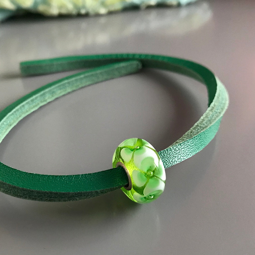 Trollbeads UNIQUES are one-of-a-kind glass beads handmade individually by 100% artisan-owned workshops. This Suzie Q Studio UNIQUES glass bead has green shamrock-style flowers that interlock with one another.