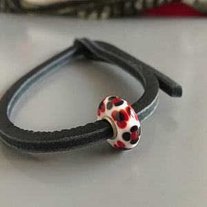  This Suzie Q Studio Trollbeads UNIQUES glass bead bracelet features the powerful and classic color-combo of red, black and white with a black leather bracelet.