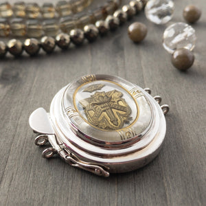 This unusual triple-strand, sterling silver box clasp features a three-dimensional, antique gold crest floating under a dome of clear glass, on a base of silver-leaf. The outer border is also 3-D, with a lovely antique gold design etched into the glass... A truly spectacular, focal-piece clasp!